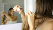 © zigres - Young woman applying oil mask to hair tips in front of a mirror. Haircare concept. Focus on hair.