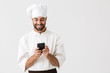 © Drobot Dean - Cheerful smiling young chef posing isolated over white wall background in uniform using mobile phone.