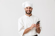 © Drobot Dean - Cheerful smiling young chef posing isolated over white wall background in uniform using mobile phone.