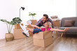 © Evrymmnt - Young married couple moving into a new home. Attractive blonde woman sitting in cardboard box, bearded man pushes her. Newely weds fooling around. Minimal interior background, copy space, close up