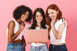 © Drobot Dean - Cute smiling young three multiethnic girls friends posing isolated over pink wall background using laptop computer.