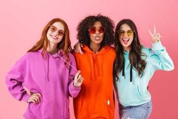 Wall Mural - Three happy young girls wearing colorful hoodies standing