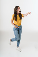 Poster - Full length image of amazed brunette woman wearing casual clothes smiling and pointing finger at copyspace