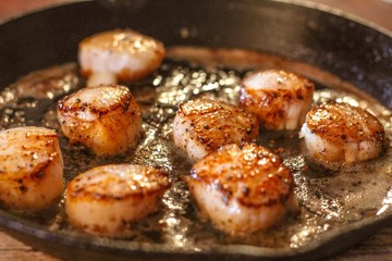 Selective Focus closeup of perfectly seared fresh sea scallops in butter and cracked pepper, sizzling on a cast iron skillet