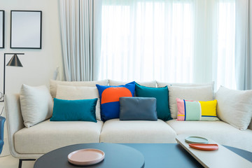 Large white sofa with colorful cushions in a spacious living room interior with green plants and white walls.