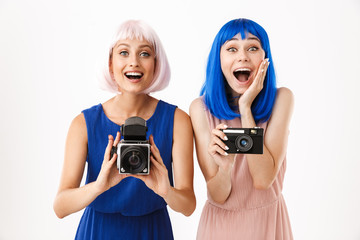 Wall Mural - Portrait of two excited women wearing blue and pink wigs taking photo on retro cameras