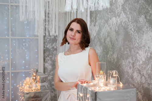 A beautiful happy woman in a white evening dress is standing near the Christmas garland and decorations Canvas