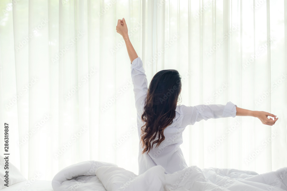 Asian women waking up stretching in bed room at home, early morning time and sunny day. Lifestyle Concept - obrazy, fototapety, plakaty 