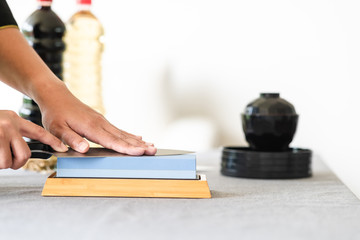 Chef sharpening knife on table. Japanese setting with asian woman. Side angle with opy space.