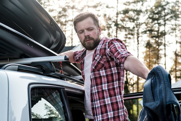 A focused man pulls things out of the roof rack of a car or in a cargo box after a family trip on vacation.