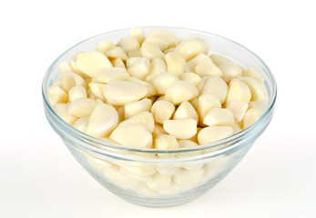 Wall Mural - Peeled garlic cloves in glass bowl, front view. Allium sativum, with pungent flavor, used as seasoning or condiment and in medicine. Macro food photo, closeup, on white background.