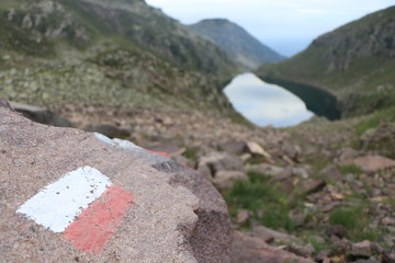 stone with red and white sign of the path with a lake as background, lago brutto in mountain, italian alps