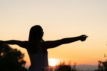 silhouette of womasilhouette of young woman with open arms raised in a sunsetn relaxing her arms at sunset