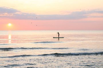 Woman's silhouette on a paddle board (SUP) at a beautiful pink pastel gradient sunset.