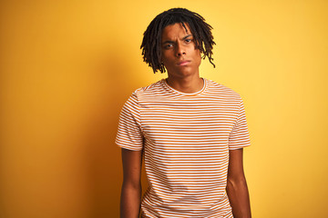 Afro man with dreadlocks wearing striped t-shirt standing over isolated yellow background skeptic and nervous, frowning upset because of problem. Negative person.