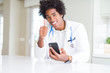 © Krakenimages.com - African American doctor man using smartphone at the clinic happy with big smile doing ok sign, thumb up with fingers, excellent sign