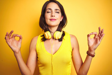 Wall Mural - Young beautiful woman wearing headphones over yellow isolated background relax and smiling with eyes closed doing meditation gesture with fingers. Yoga concept.