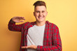 © Krakenimages.com - Young handsome man wearing casual shirt standing over isolated yellow background gesturing with hands showing big and large size sign, measure symbol. Smiling looking at the camera. Measuring concept.