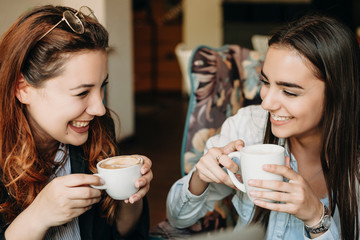 Two beautiful woman drinking coffee and laughing while storytelling while sitting in a cafe.