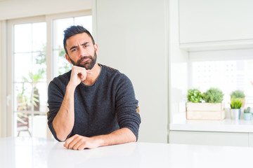 Canvas Print - Handsome hispanic man wearing casual sweater at home with hand on chin thinking about question, pensive expression. Smiling with thoughtful face. Doubt concept.