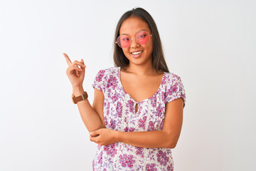 Young chinese woman wearing floral t-shirt and pink glasses over isolated white background with a big smile on face, pointing with hand and finger to the side looking at the camera.