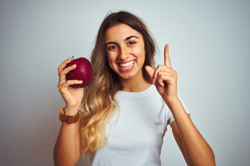 Canvas Print - Young beautiful woman eating red apple over grey isolated background surprised with an idea or question pointing finger with happy face, number one