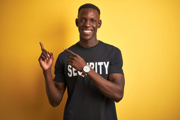 African american safeguard man wearing security uniform over isolated yellow background smiling and looking at the camera pointing with two hands and fingers to the side.