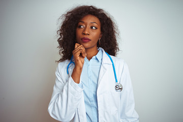 Young african american doctor woman wearing stethoscope over isolated white background with hand on chin thinking about question, pensive expression. Smiling with thoughtful face. Doubt concept.