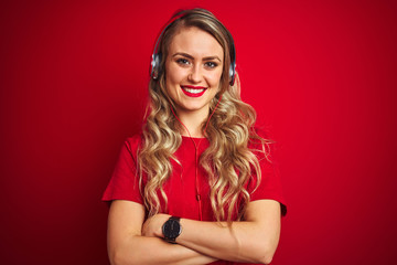 Young beautiful woman wearing headphones over red isolated background happy face smiling with crossed arms looking at the camera. Positive person.