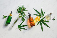 Various Glass Bottles With CBD Oil, THC Tincture And Hemp Leaves On A Marble Background. Flat Lay, Minimalism. Cosmetics CBD Oil.