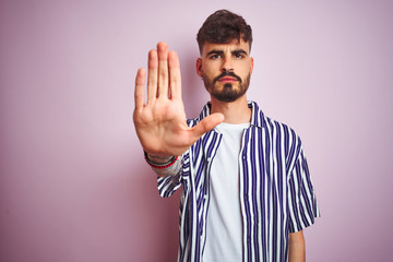 Poster - Young man with tattoo wearing striped shirt standing over isolated pink background doing stop sing with palm of the hand. Warning expression with negative and serious gesture on the face.