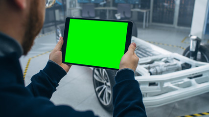 Engineer with Glasses and Beard Scans Electric Car Chassis Prototype with Wheels, Batteries and Engine with an Augmented Reality Software on a Tablet Computer in a High Tech Development Laboratory.