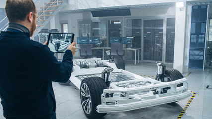 Poster - Engineer with Glasses and Beard Scans Electric Car Chassis Prototype with Wheels, Batteries and Engine with an Augmented Reality Software on a Tablet Computer in a High Tech Development Laboratory.