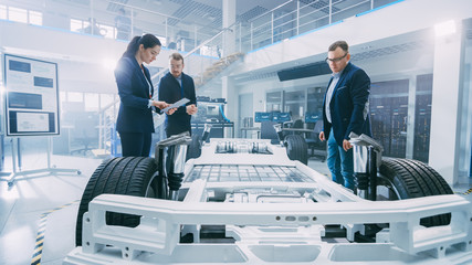 Fototapete - Automotive Design Engineers Talking while Working on Electric Car Chassis Prototype. In Innovation Laboratory Facility Concept Vehicle Frame Includes Wheels, Suspension, Engine and Battery.