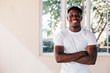© twinsterphoto - Cheerful African American sportsman in white t shirt standing with crossed arms smiling and looking at camera by window in gym