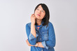 © Krakenimages.com - Young beautiful chinese woman wearing denim shirt over isolated white background with hand on chin thinking about question, pensive expression. Smiling with thoughtful face. Doubt concept.