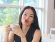 © Phuttharak - Asian woman making kissing and funny face with cup of coffee in her hands.