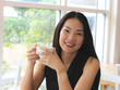 © Phuttharak - Asian woman holding cup of coffee smiling and looking to the camera.