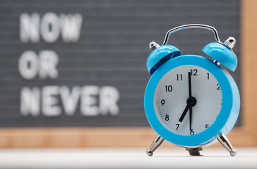 blue analog alarm clock on English text background now or never . the concept of immediate action