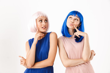 Wall Mural - Portrait of two nice women wearing blue and pink wigs dreaming while looking upward at copyspace