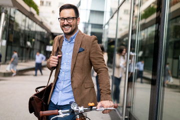 Happy young stylish businessman going to work by bike