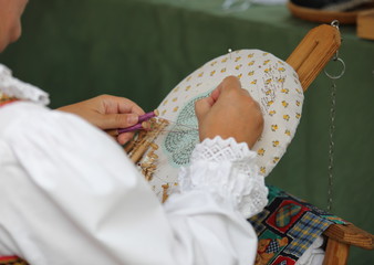 Woman in white folk shirt embroiders traditional pattern on special kind of canvas, close up