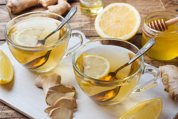 Two cups of natural herbal tea ginger lemon and honey on a wooden background.