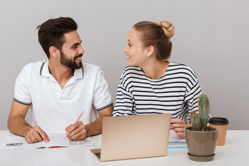 Poster - Loving couple friends man and woman sitting at the table indoors isolated over grey background using laptop computer reading book studying.