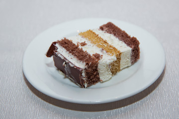 Wall Mural - Close-up shot. Free space for text.Slice of chocolate cake white cream on plate. Chocolate cake with whipped cream . A slice of cake in a white plate on a white wooden table with a spoon.