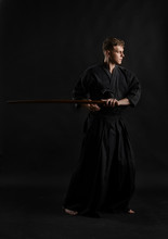 Kendo Guru Wearing In A Traditional Japanese Kimono Is Practicing Martial Art With The Shinai Bamboo Sword Against A Black Studio Background.