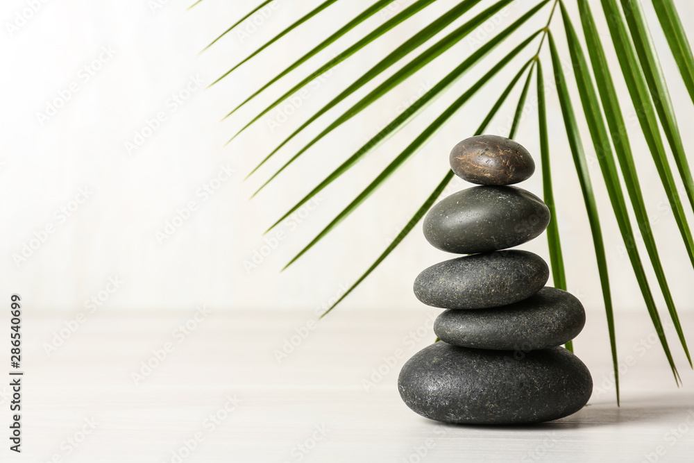Stack of spa stones and palm leaf on table against white background, space for text - obrazy, fototapety, plakaty 