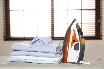 Poster - Modern electric iron and folded clothes on board in room