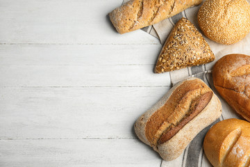 Loaves of different breads on white wooden background, flat lay. Space for text