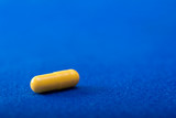 Fototapeta  - One yellow medical pill. Color capsule medication. Blue background. Health care concept. Free space for text. Medicines. Chemical industry.